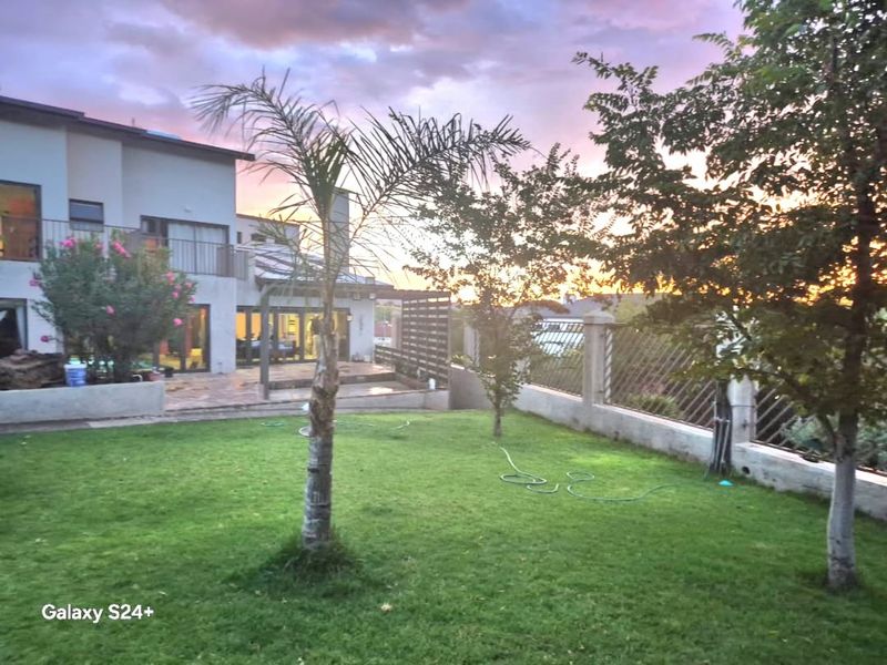 A view of the rear garden featuring a paved patio area, pergola, and established boundary wall at sunset.