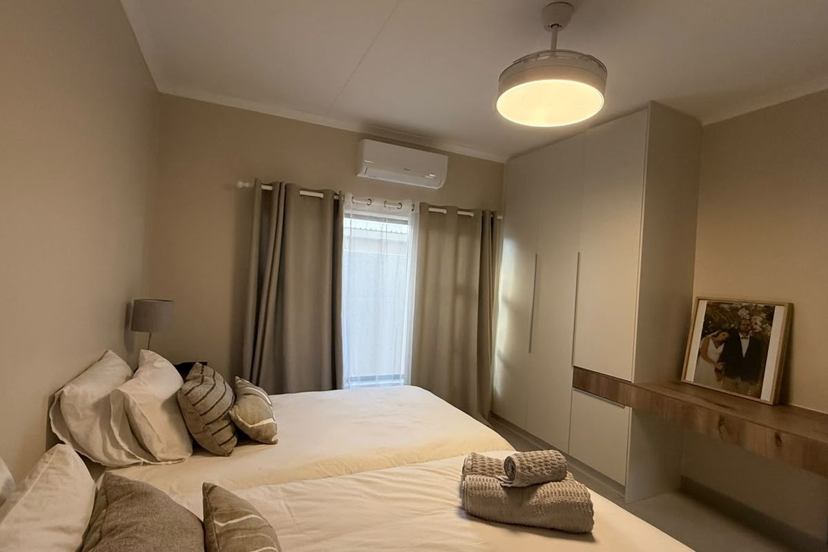 A well-maintained bedroom featuring built-in cupboards, a floating vanity shelf, and a wall-mounted air conditioning unit for climate control.