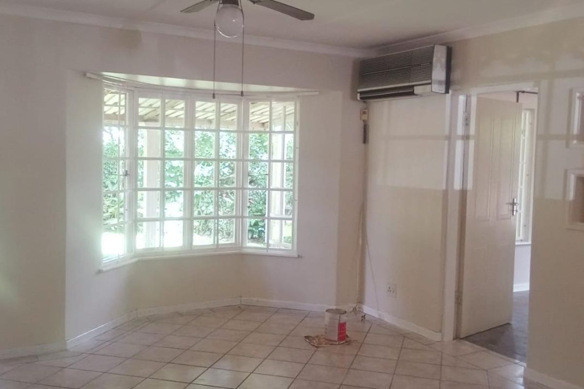 An empty living room featuring tiled flooring, a bay window, a ceiling fan, and a wall-mounted air conditioning unit.
