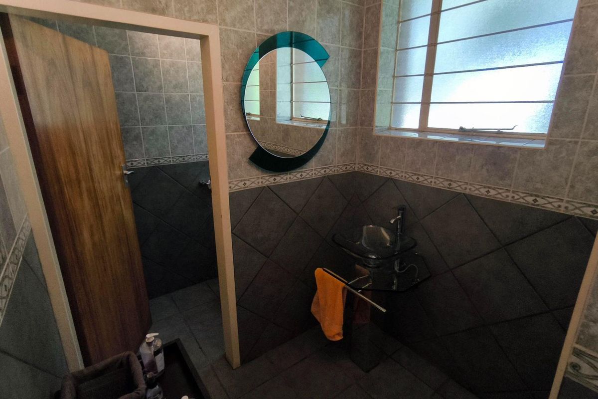 A compact bathroom featuring tiled walls and flooring, a modern glass vessel sink with wall-mounted faucet, and a decorative circular mirror.