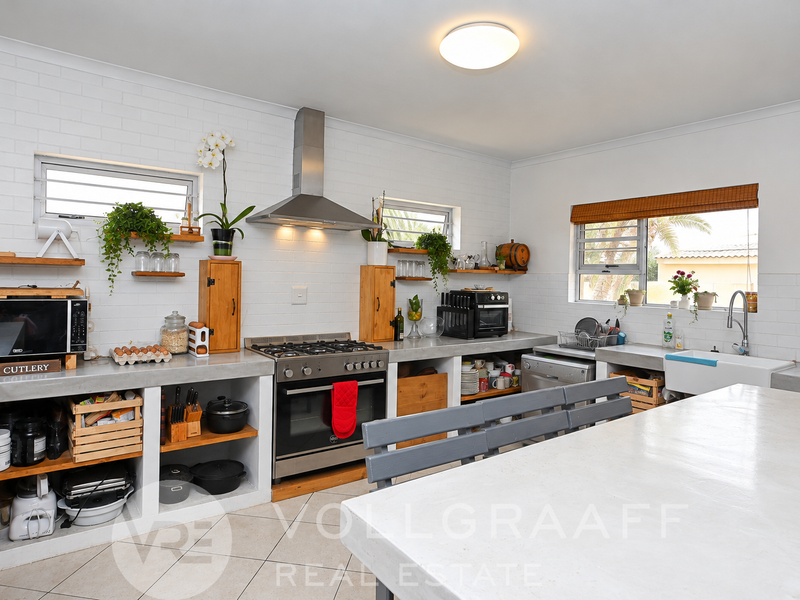 A rustic-style kitchen featuring concrete countertops, a farmhouse sink, gas stove with extractor fan, and open shelving with a brick-textured wall finish.