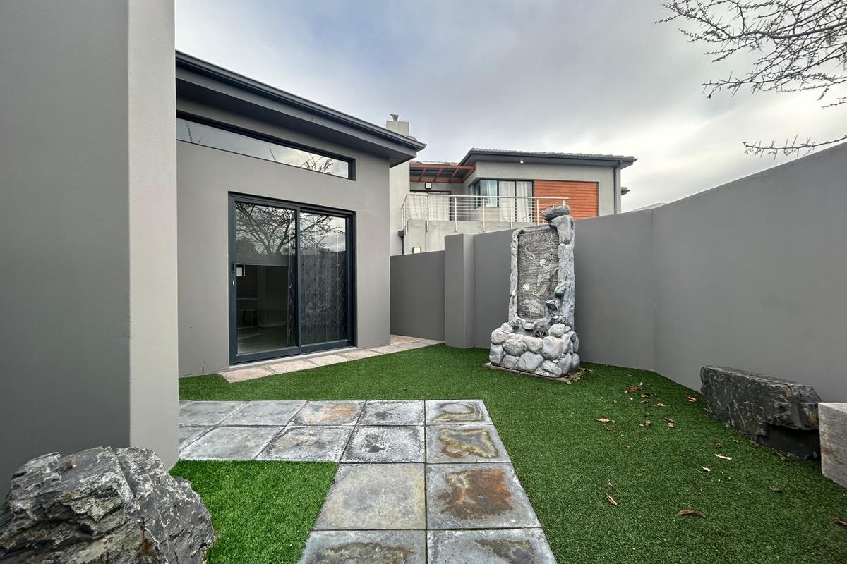 A private rear courtyard featuring artificial turf, stone paving, a decorative water feature, and a modern sliding glass door providing access to the home.