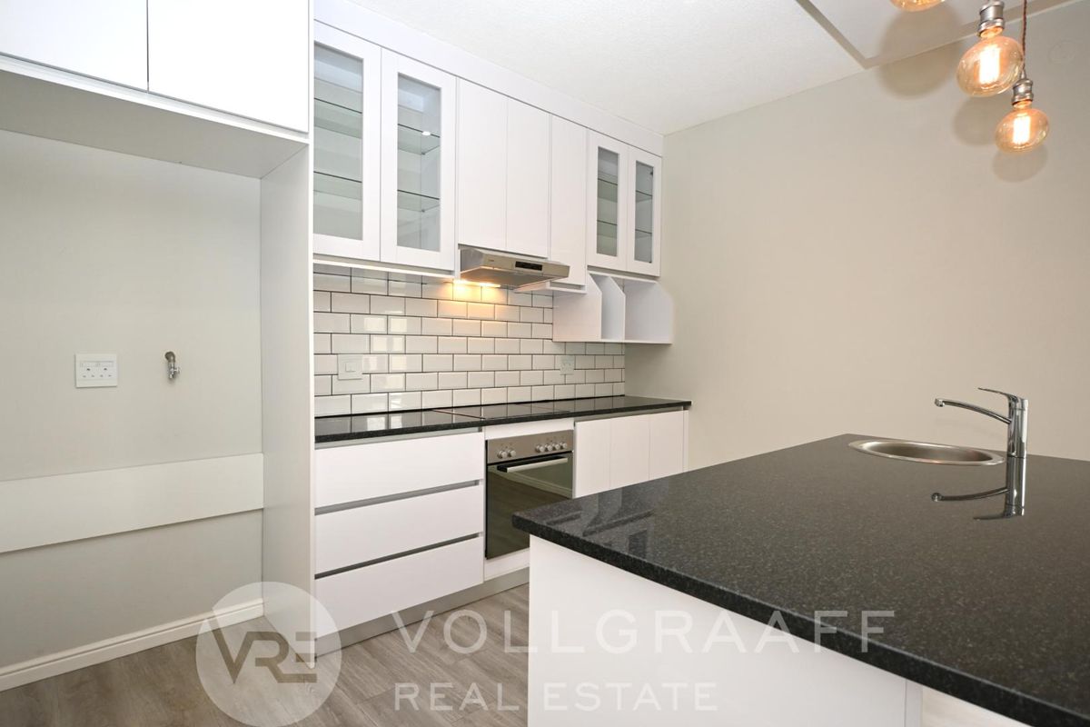 Modern kitchen featuring white cabinetry, black granite countertops, subway tile backsplash, built-in oven, extractor fan, and a central island with a sink.