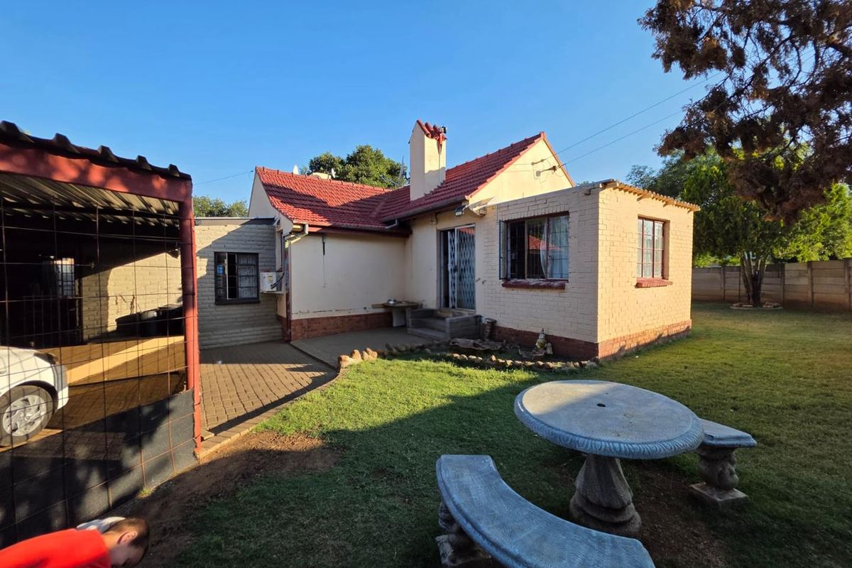 Rear view of the property featuring a brick facade, tiled roof, chimney, and an attached paved patio area overlooking the garden.
