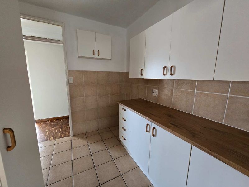 A functional scullery or utility area featuring white built-in cabinetry, a wood-look laminate countertop, and neutral tiled finishes.