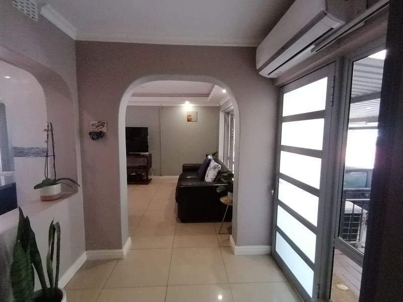 A well-maintained living area featuring tiled flooring, a decorative archway, and a wall-mounted split-system air conditioner, leading to an outdoor space.