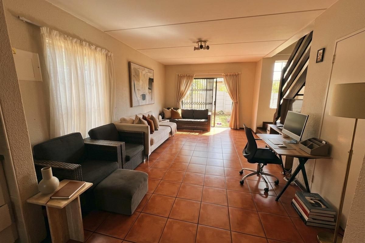 Spacious living area featuring terracotta-style tiled flooring, a staircase, and a sliding glass door providing access to the rear outdoor space.