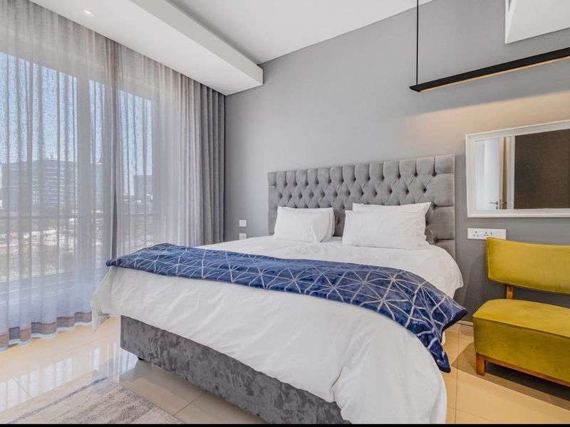 A modern, well-maintained bedroom featuring tiled floors, recessed ceiling lighting, and a large sliding glass door providing access to a balcony.