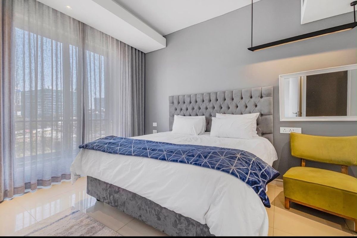 A modern, well-maintained bedroom featuring tiled floors, recessed ceiling lighting, and a large sliding glass door providing access to a balcony.