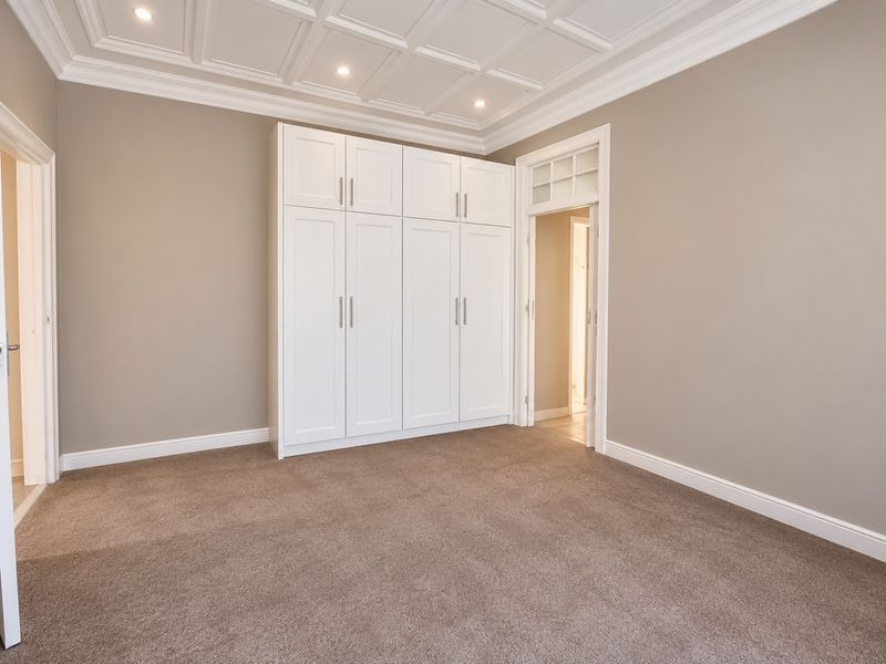 A spacious, well-maintained bedroom featuring elegant coffered ceilings, recessed lighting, and ample built-in cupboard storage with neutral carpeting.