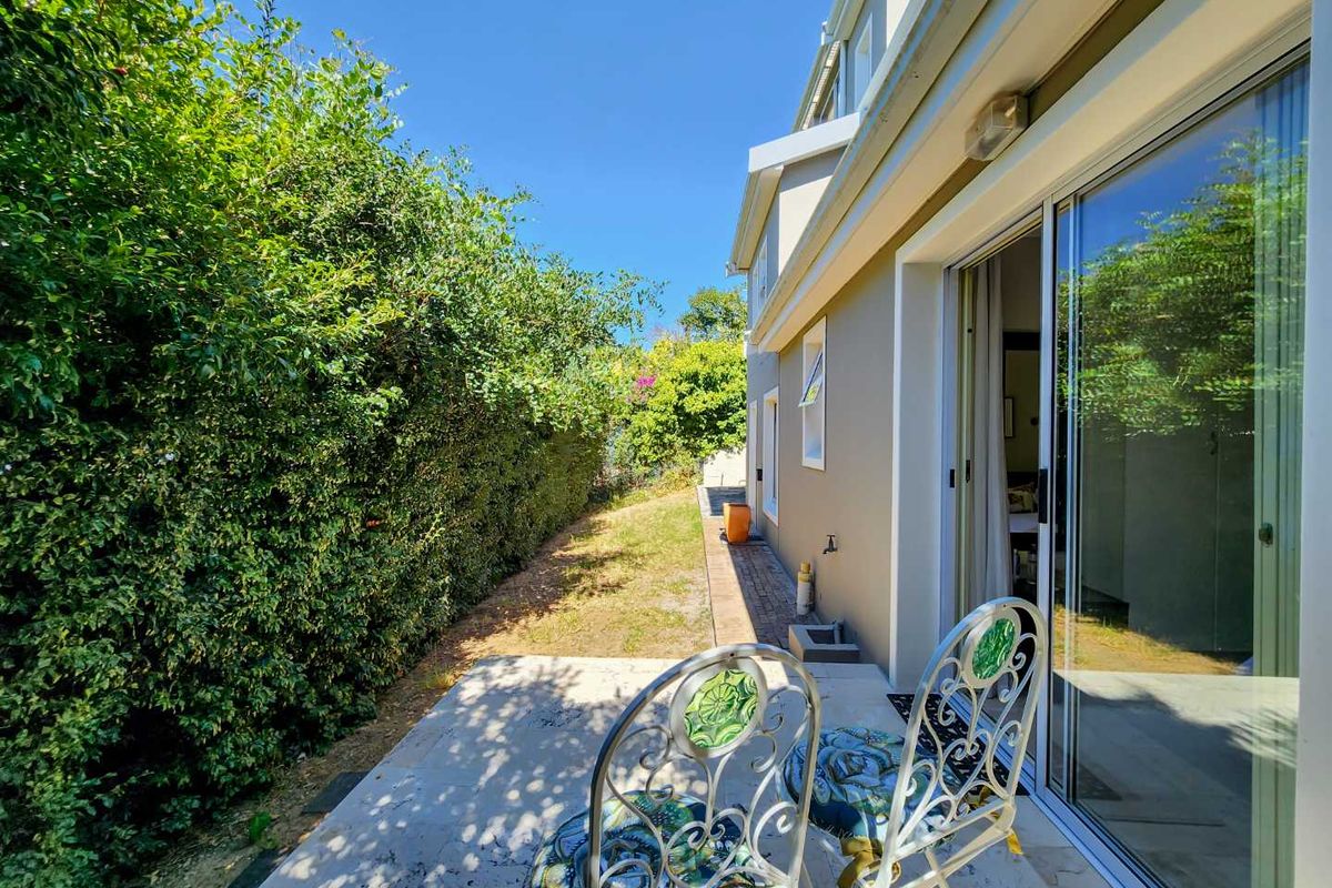 Rear exterior view of the townhouse featuring a paved patio area, sliding glass doors, and a side garden with established hedging.