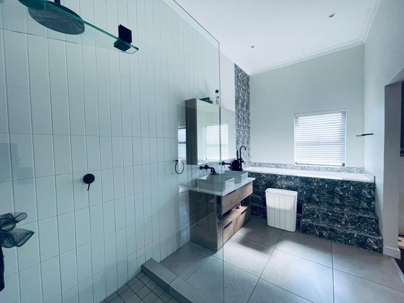 Modern bathroom featuring a walk-in shower with glass screen, double vanity, and a tiled built-in bathtub with contemporary finishes.