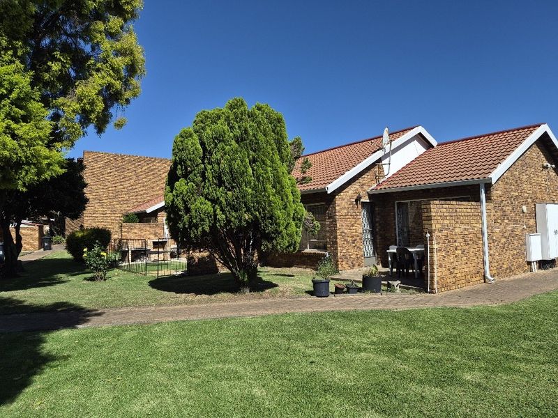 A view of the rear exterior of the apartment, featuring a face brick facade, tiled roof, and a well-maintained garden with a paved walkway.