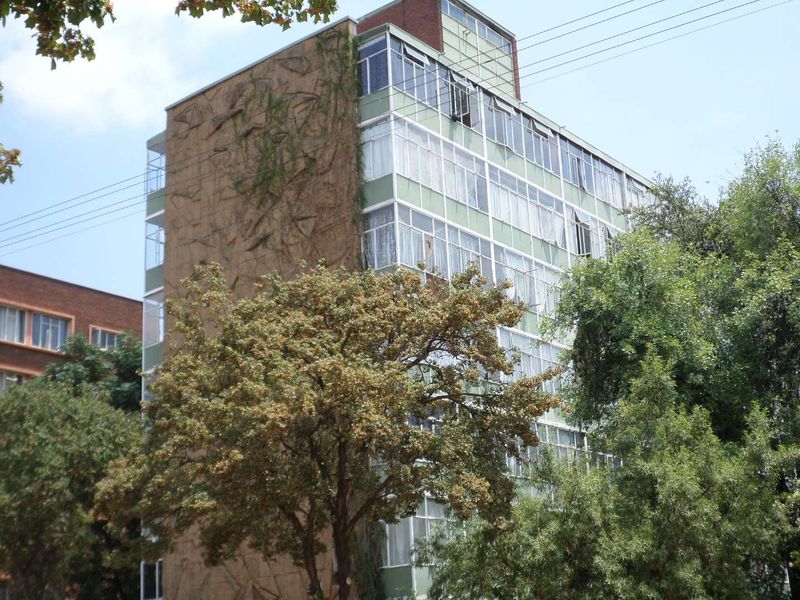 Exterior view of a multi-story apartment building featuring large windows and textured facade detailing, surrounded by mature trees.