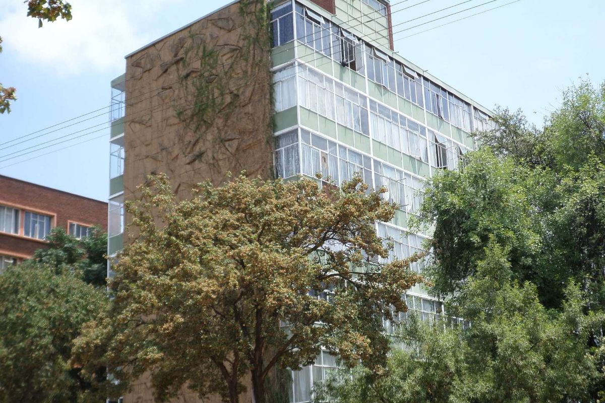 Exterior view of a multi-story apartment building featuring large windows and textured facade detailing, surrounded by mature trees.