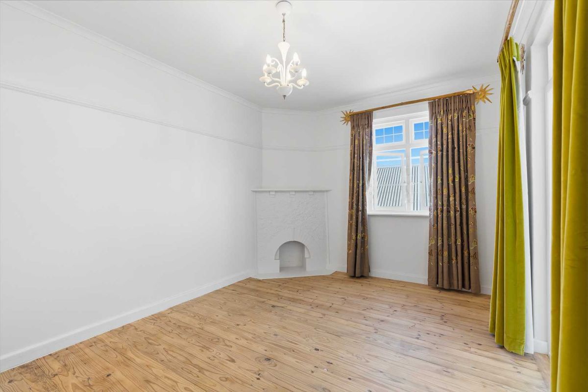 A bright bedroom featuring polished timber flooring, a decorative corner fireplace, and a classic chandelier, offering a clean and neutral living space.