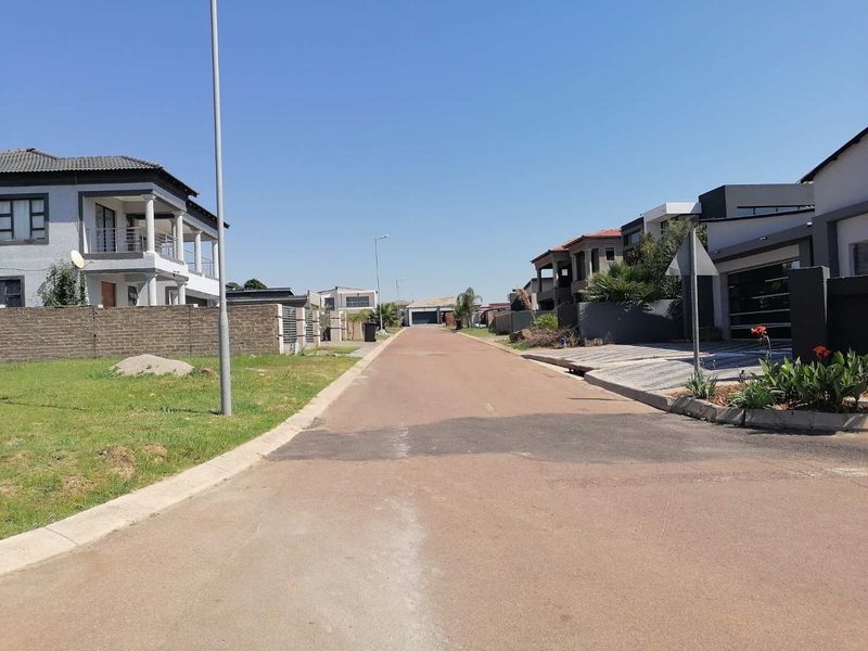 A clear street view of a modern residential neighbourhood featuring paved roads, concrete kerbing, and established boundary walls.