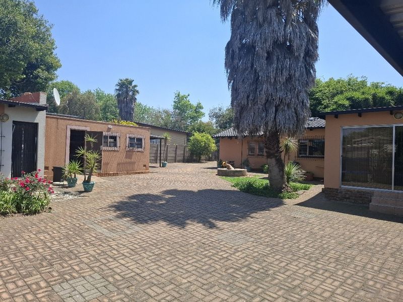 A spacious paved rear courtyard area featuring brick exterior walls, security bars on windows, and a large mature tree.