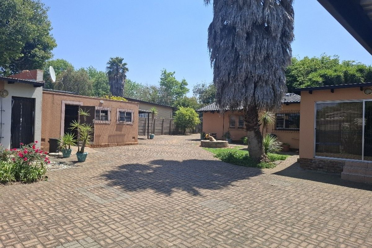 A spacious paved rear courtyard area featuring brick exterior walls, security bars on windows, and a large mature tree.