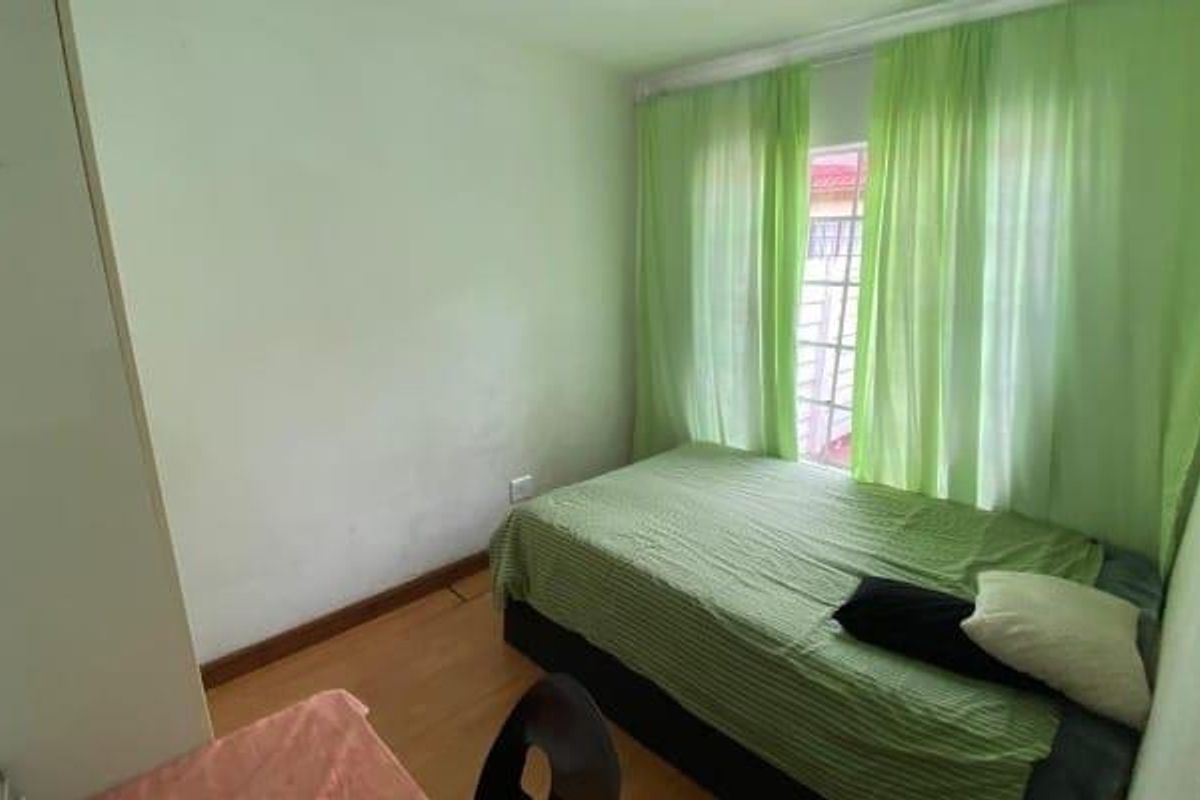 A compact bedroom featuring laminate flooring and a window with light-filtering curtains.