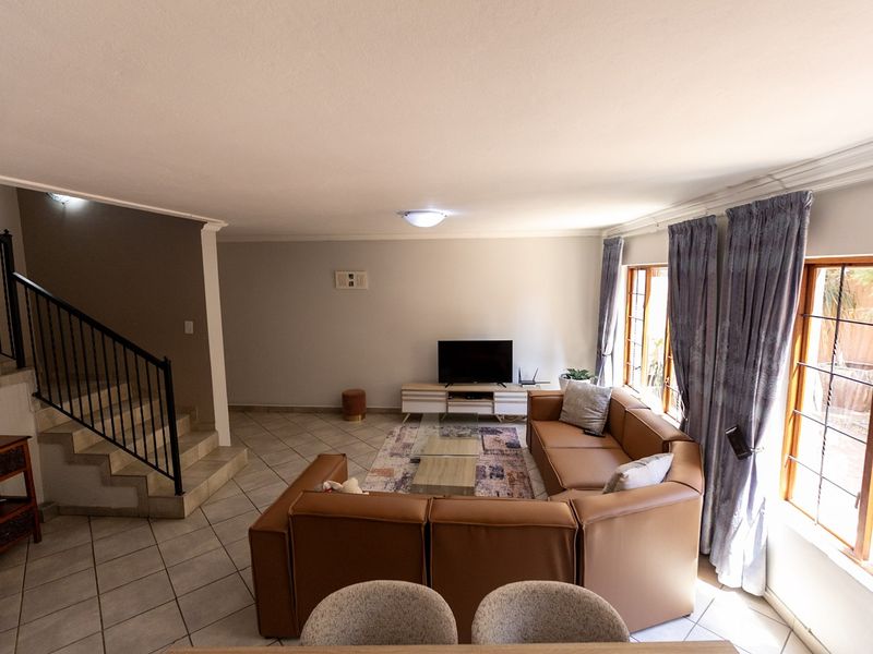 Spacious living room featuring tiled flooring, a staircase with a metal balustrade, and large windows allowing for natural light.