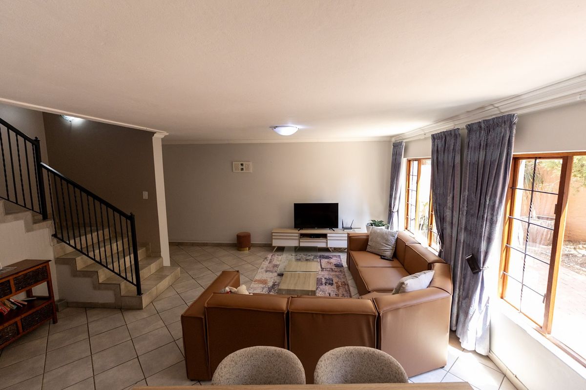 Spacious living room featuring tiled flooring, a staircase with a metal balustrade, and large windows allowing for natural light.