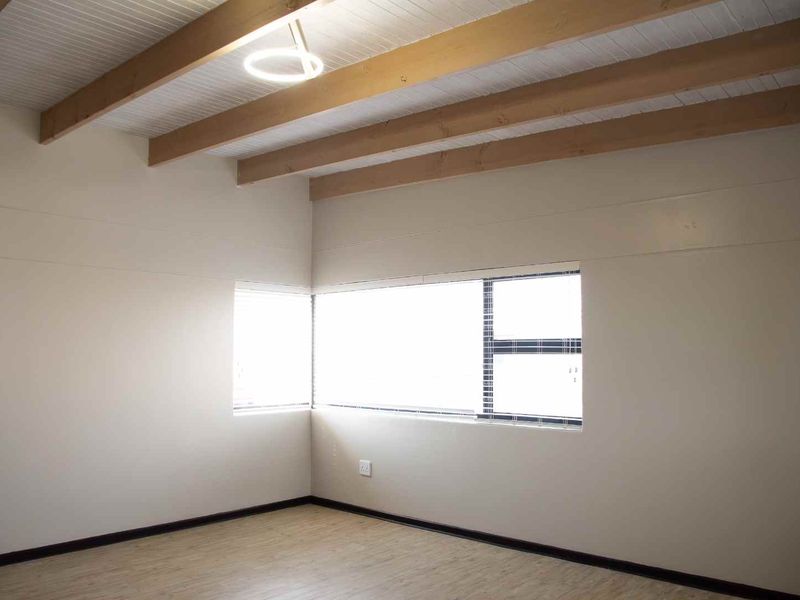 Spacious living area featuring exposed timber ceiling beams, corner windows providing natural light, and neutral laminate flooring.