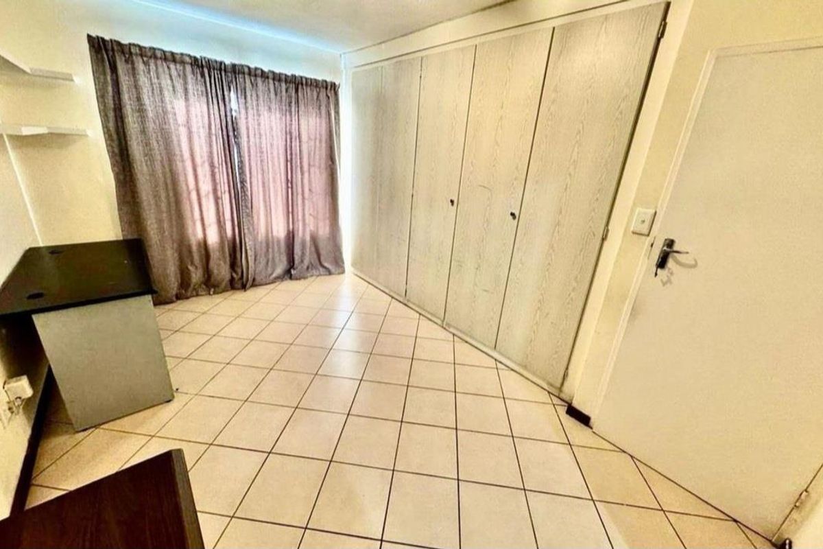 A bedroom featuring built-in cupboards, tiled flooring, and a window with curtains, offering a functional space for rest or study.