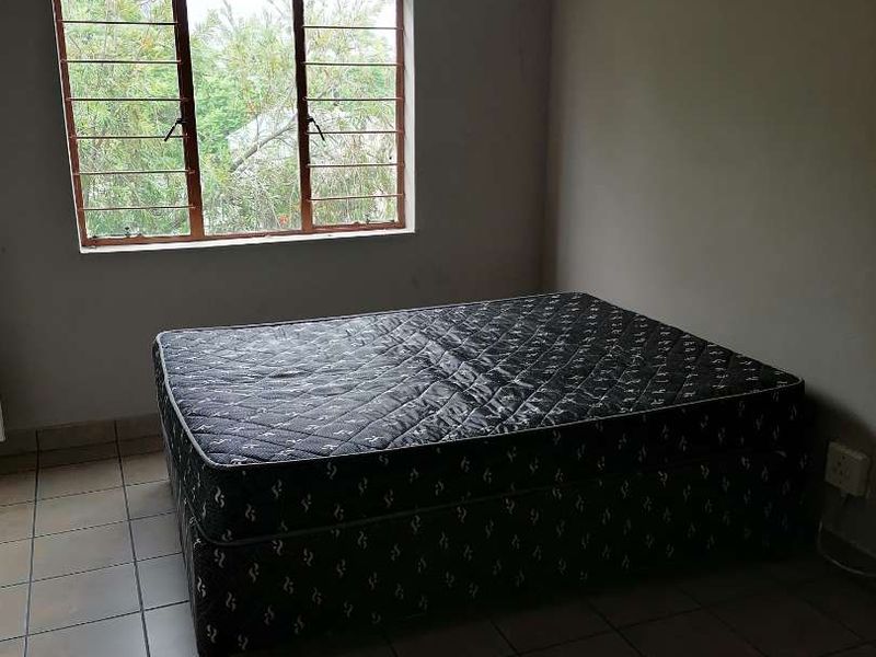 A simple bedroom featuring tiled flooring and a window with security bars, requiring minor cosmetic updates to improve its overall appeal.