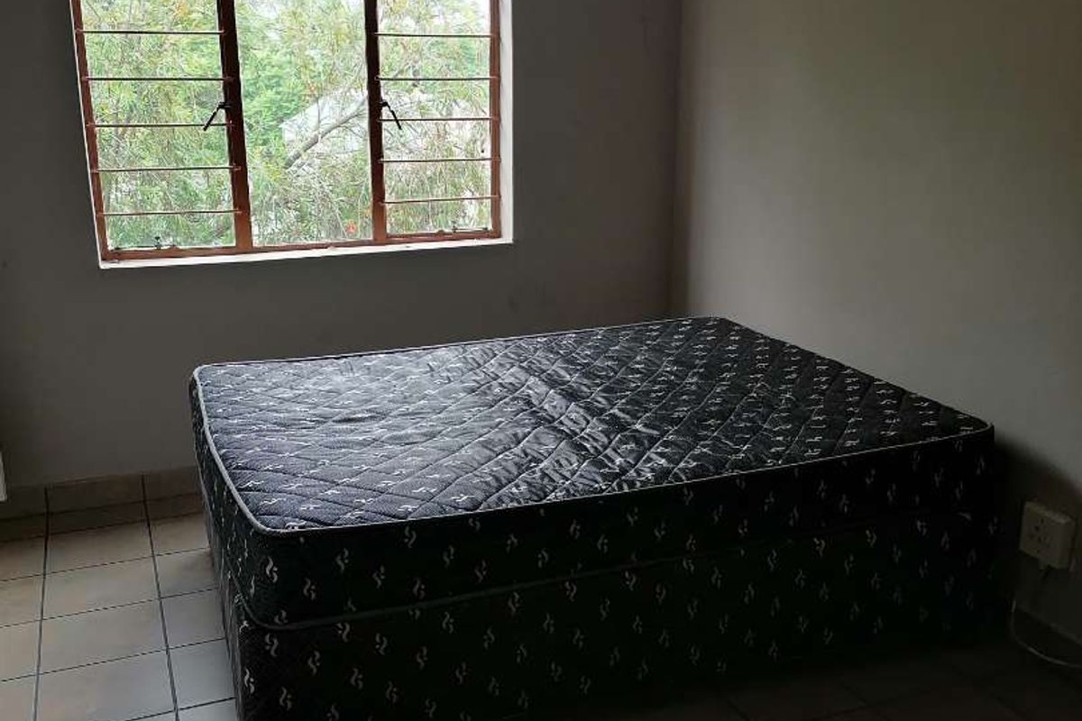 A simple bedroom featuring tiled flooring and a window with security bars, requiring minor cosmetic updates to improve its overall appeal.