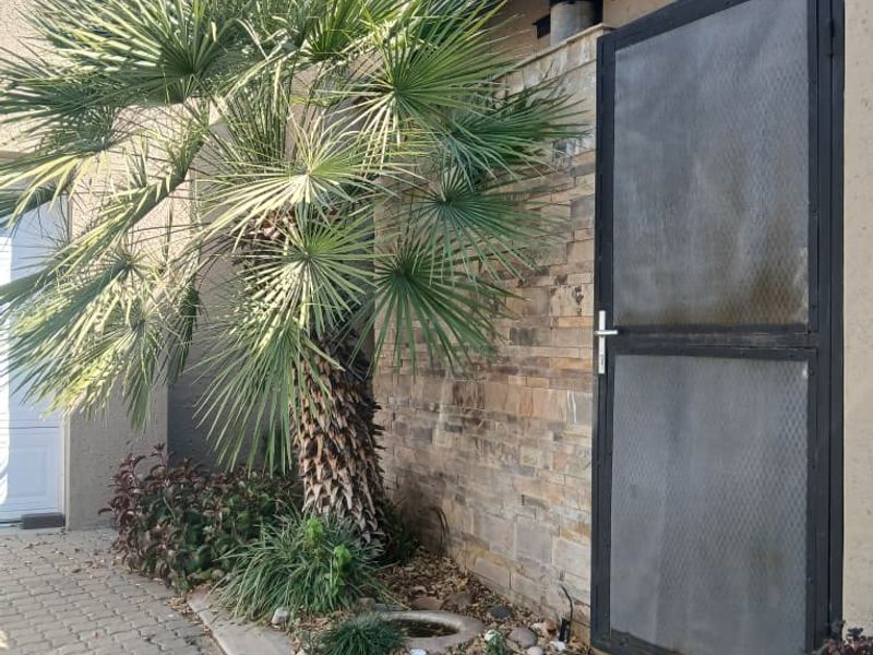 Front exterior view of the townhouse featuring stone cladding, a security gate, and paved driveway access.