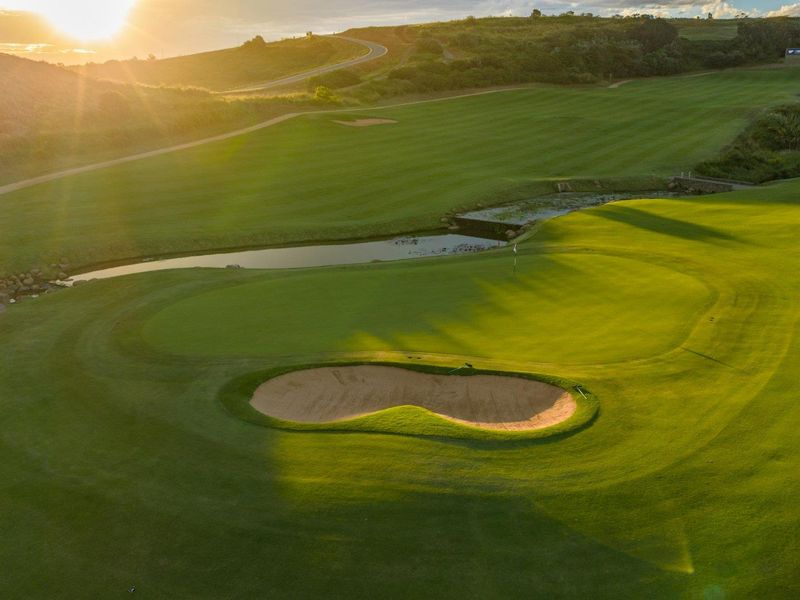Aerial view of a well-maintained golf course featuring a sand bunker and water hazard at sunset.