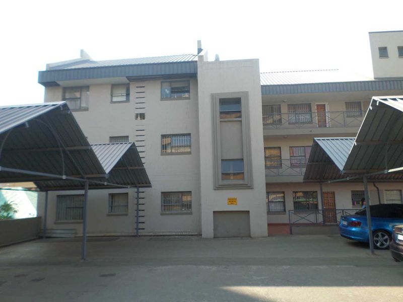 Exterior view of an apartment building featuring covered parking carports and multi-level balconies with security bars.