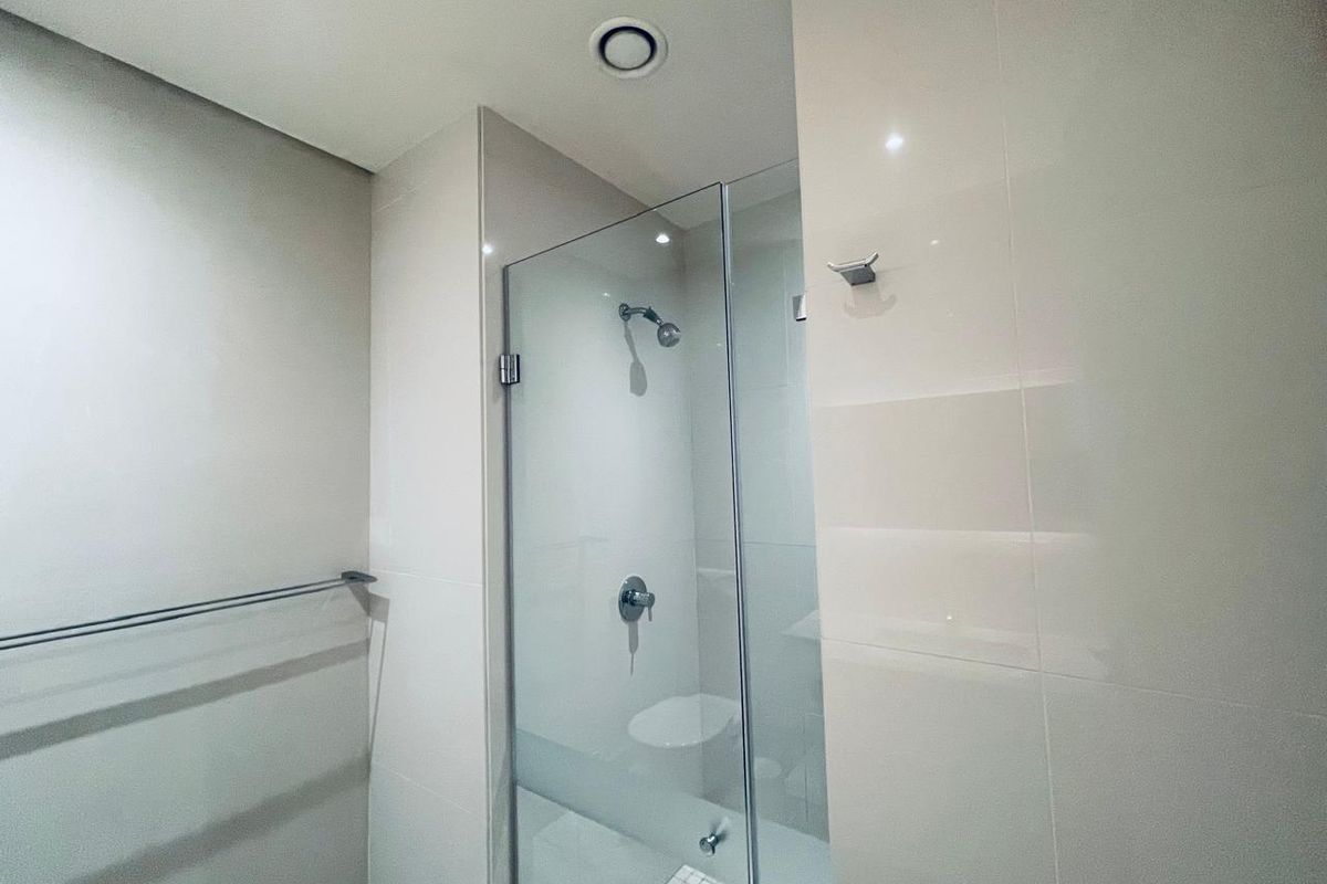 A modern, clean bathroom featuring a glass-enclosed shower with neutral wall tiling and mosaic floor detailing.