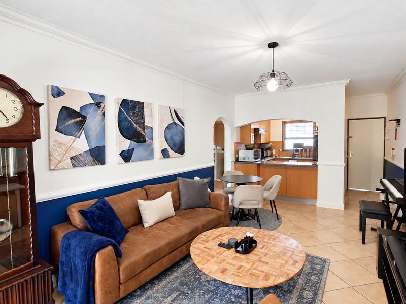 Open plan living area featuring tiled floors, crown molding, and a connected kitchen space with wooden cabinetry and a breakfast counter.