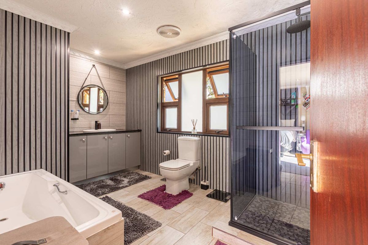 Modern bathroom featuring a vanity with basin, toilet, separate shower enclosure, and a bathtub, finished with contemporary wall paneling and tiled flooring.
