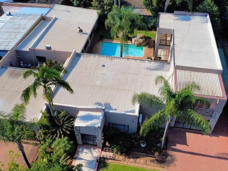 Aerial view of the property featuring a large corrugated metal roof, a swimming pool, and paved driveway areas surrounded by established palm trees.