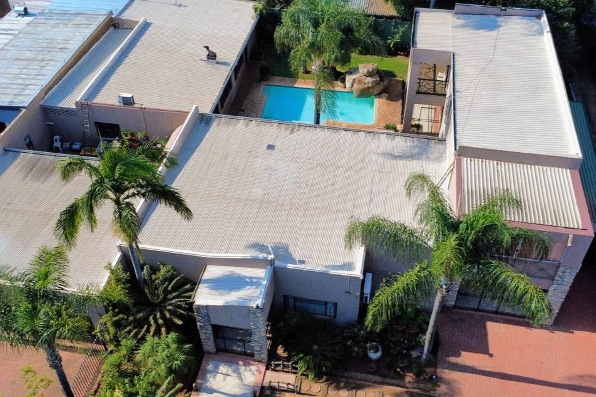 Aerial view of the property featuring a large corrugated metal roof, a swimming pool, and paved driveway areas surrounded by established palm trees.