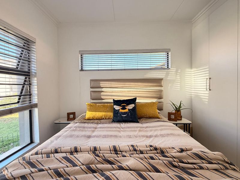 A well-lit bedroom featuring built-in cupboards, modern venetian blinds, and neutral finishes, creating a bright and comfortable living space.
