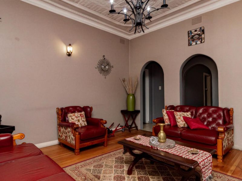 A spacious living room featuring classic archways, ornate ceiling detailing, hardwood flooring, and elegant lighting fixtures.