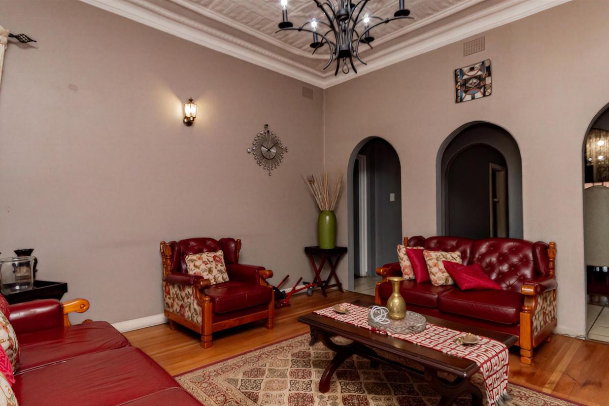 A spacious living room featuring classic archways, ornate ceiling detailing, hardwood flooring, and elegant lighting fixtures.