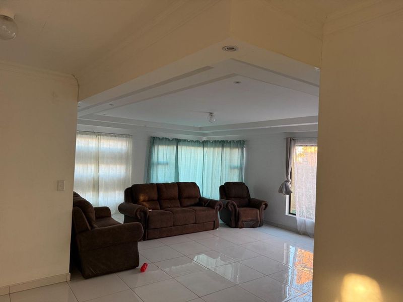 Spacious living room featuring large format floor tiles, a recessed ceiling design with downlights, and ample natural light through multiple windows.