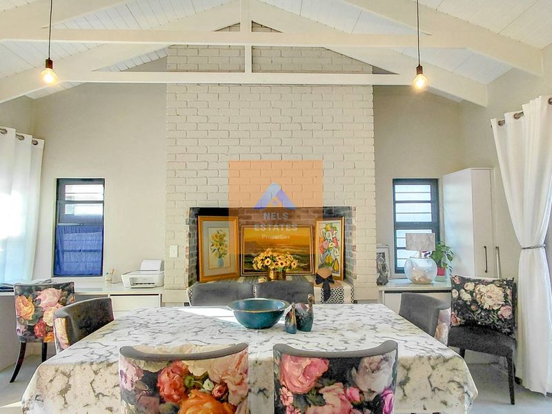 Spacious living area featuring a vaulted ceiling with exposed timber trusses and a central painted brick fireplace, offering a bright and airy atmosphere.