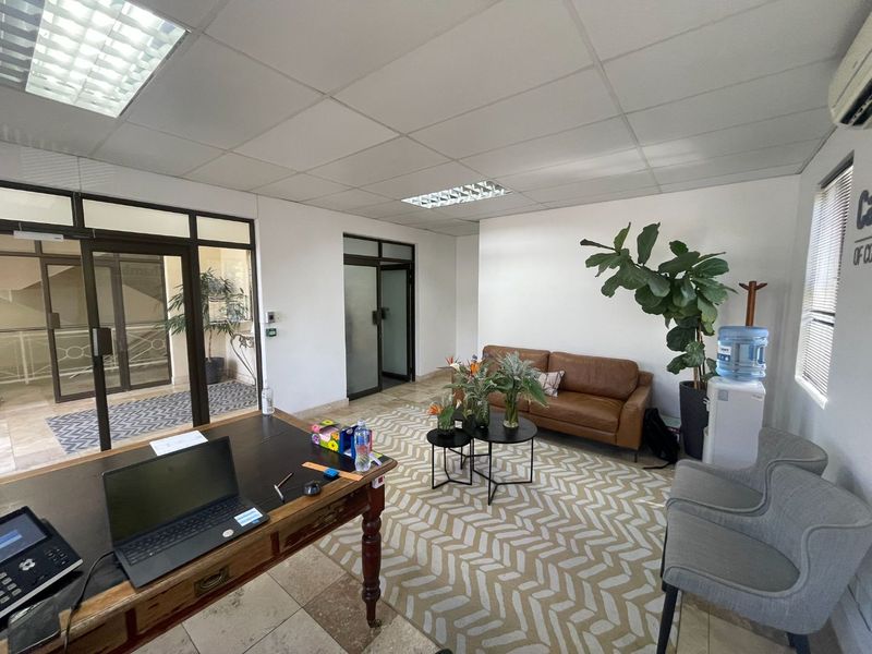 A professional office space featuring tiled flooring, a suspended ceiling with recessed lighting, and glass partition doors, providing a bright and functional work environment.
