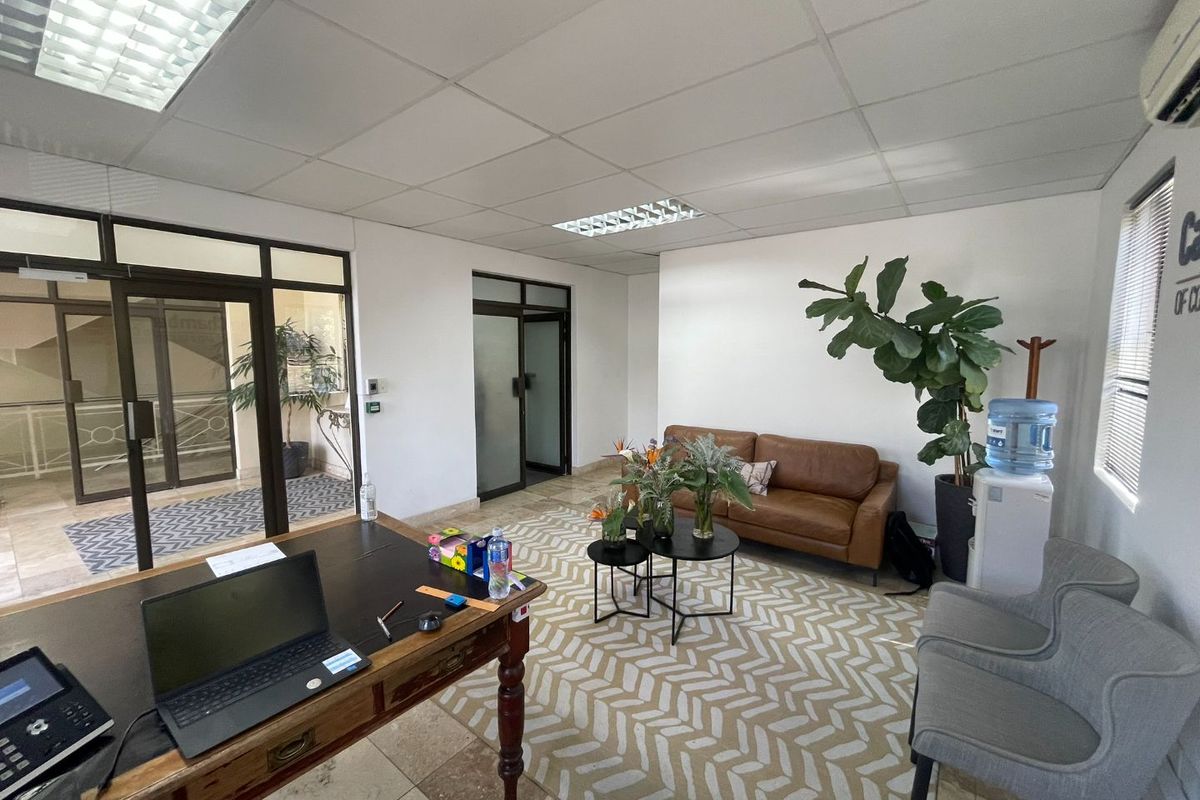 A professional office space featuring tiled flooring, a suspended ceiling with recessed lighting, and glass partition doors, providing a bright and functional work environment.