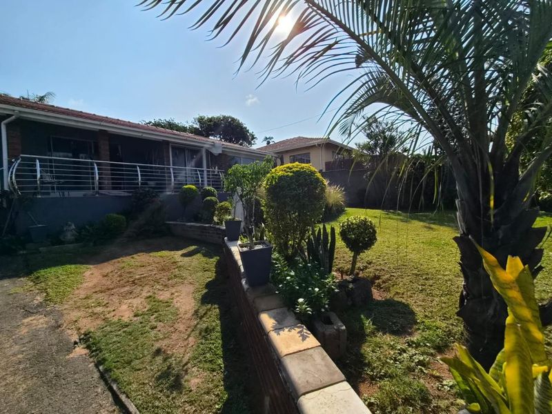 Rear view of the property featuring a raised patio with stainless steel balustrades, overlooking a landscaped garden with a brick retaining wall.