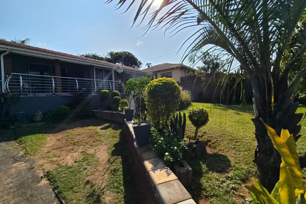 Rear view of the property featuring a raised patio with stainless steel balustrades, overlooking a landscaped garden with a brick retaining wall.