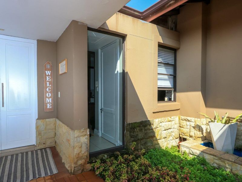 A welcoming entrance area featuring double doors, stone cladding accents, a built-in water feature, and a skylight providing natural light.