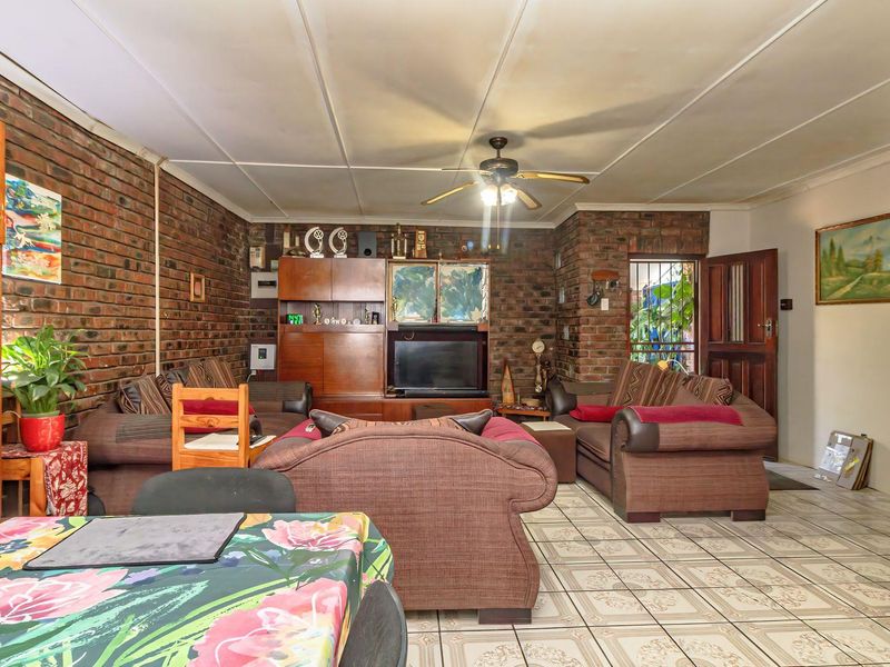 Living room featuring exposed brick walls, tiled flooring, and a ceiling fan, offering a rustic aesthetic with potential for modern updates.