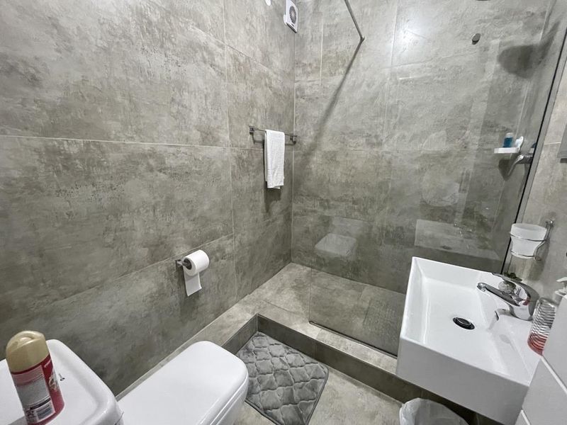 Modern bathroom featuring large-format grey wall tiles, a walk-in shower with a glass screen, a wall-mounted basin, and a toilet.